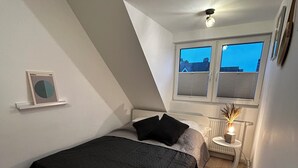 A bedroom with a bed, a bedside table with a lamp, a radiator, and a window with blinds. - Fisherman's chic "Die Bude" at the port of Maasholm (Maasholm)