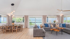 Un salón amplio con un gran ventanal, una zona de comedor y un sofá gris con cojines azules.