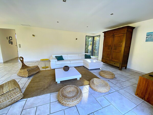 A modern living room with a white sofa, a wooden cabinet, wicker furniture, and a tiled floor.