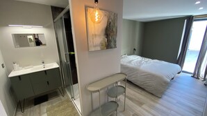 Ein modernes Schlafzimmer mit einem großen Bett, einem Nachttisch, einem Spiegel und einem Duschbereich.
