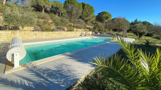 Ein Pool mit Steinmauer und Liegestühlen, umgeben von Bäumen und Grünpflanzen.