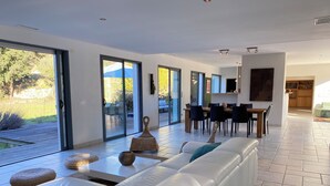 Ein modernes Wohnzimmer mit einem weißen Sofa, einem Essbereich und großen Schiebegläsern, die auf eine Terrasse führen.