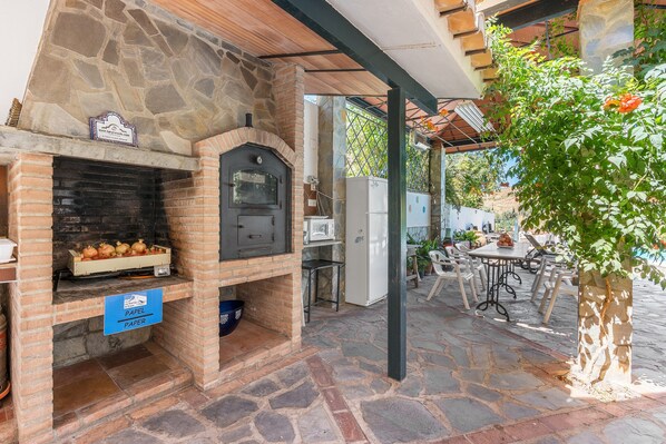An outdoor stone fireplace with a sign, a table with chairs, and a potted plant.