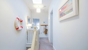 Een gang met een witte leuning, een reddingsboei als decoratie, een spiegel en een ingelijst schilderij aan de muur.