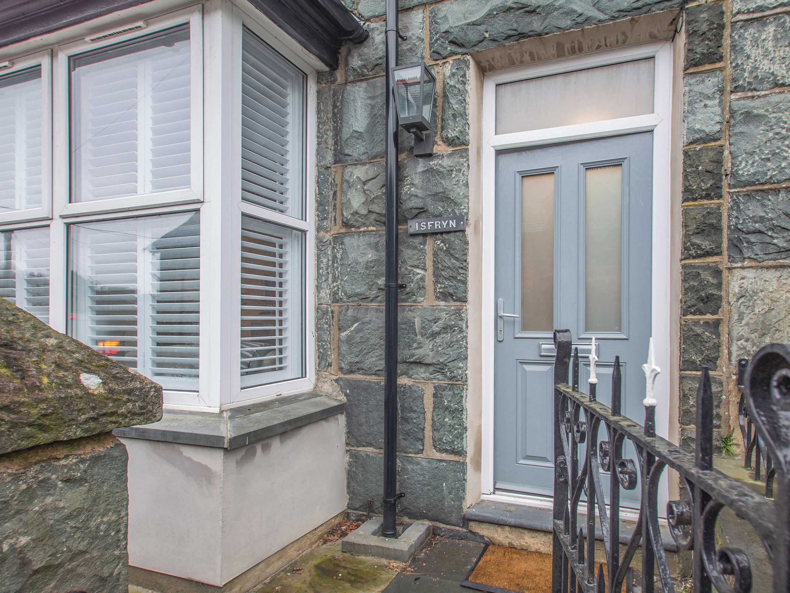 A stone facade with a grey door and white window shutters.