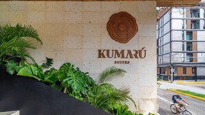 Een hotelentree met een bord waarop 'KUMARU SUITES' staat en een groot houten decoratief element erboven.