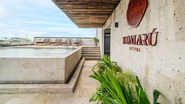 Een modern buitenzwembad met ligbedden, een betonnen zwembad en een bordje met de tekst 'KUMARÚ SUITES'.