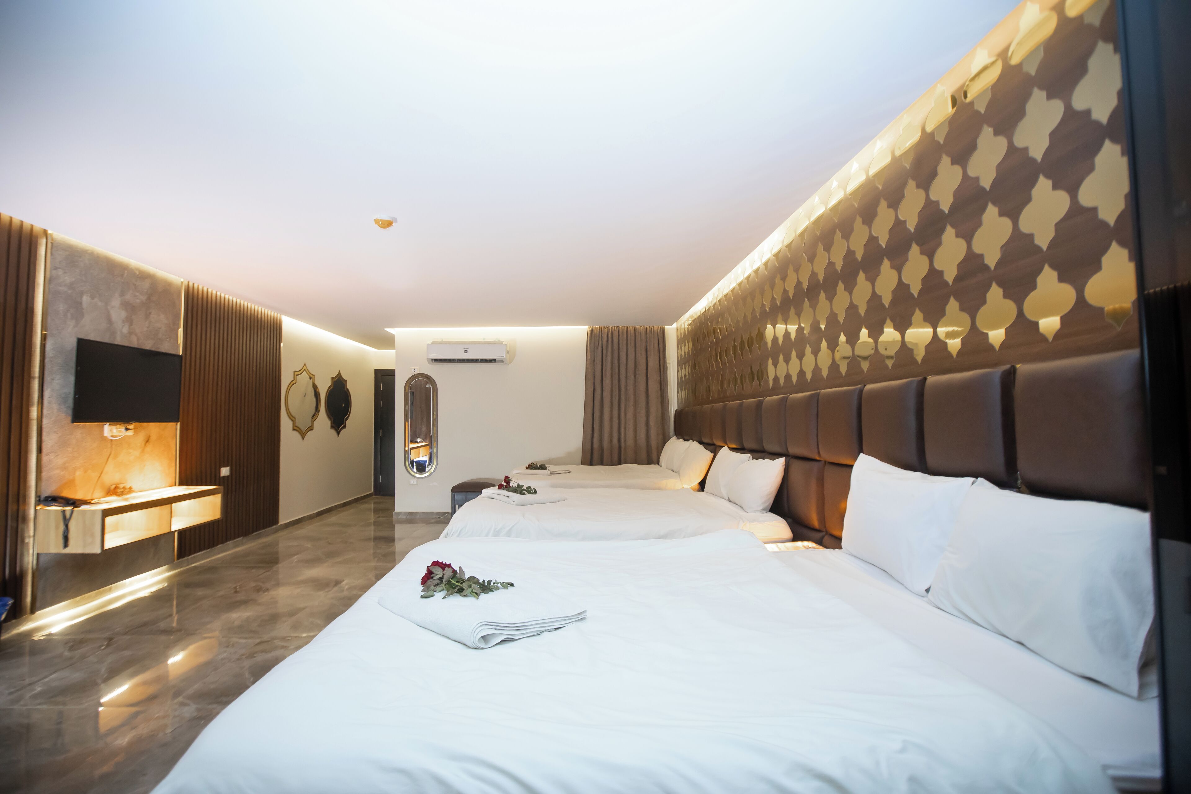 Hotellihuone, jossa on kaksi sänkyä, peilillä varustettu meikkipöytä ja seinään asennettu ilmastointilaite.