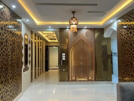 A hallway with ornate wall panels, a decorative ceiling light, and a patterned door.