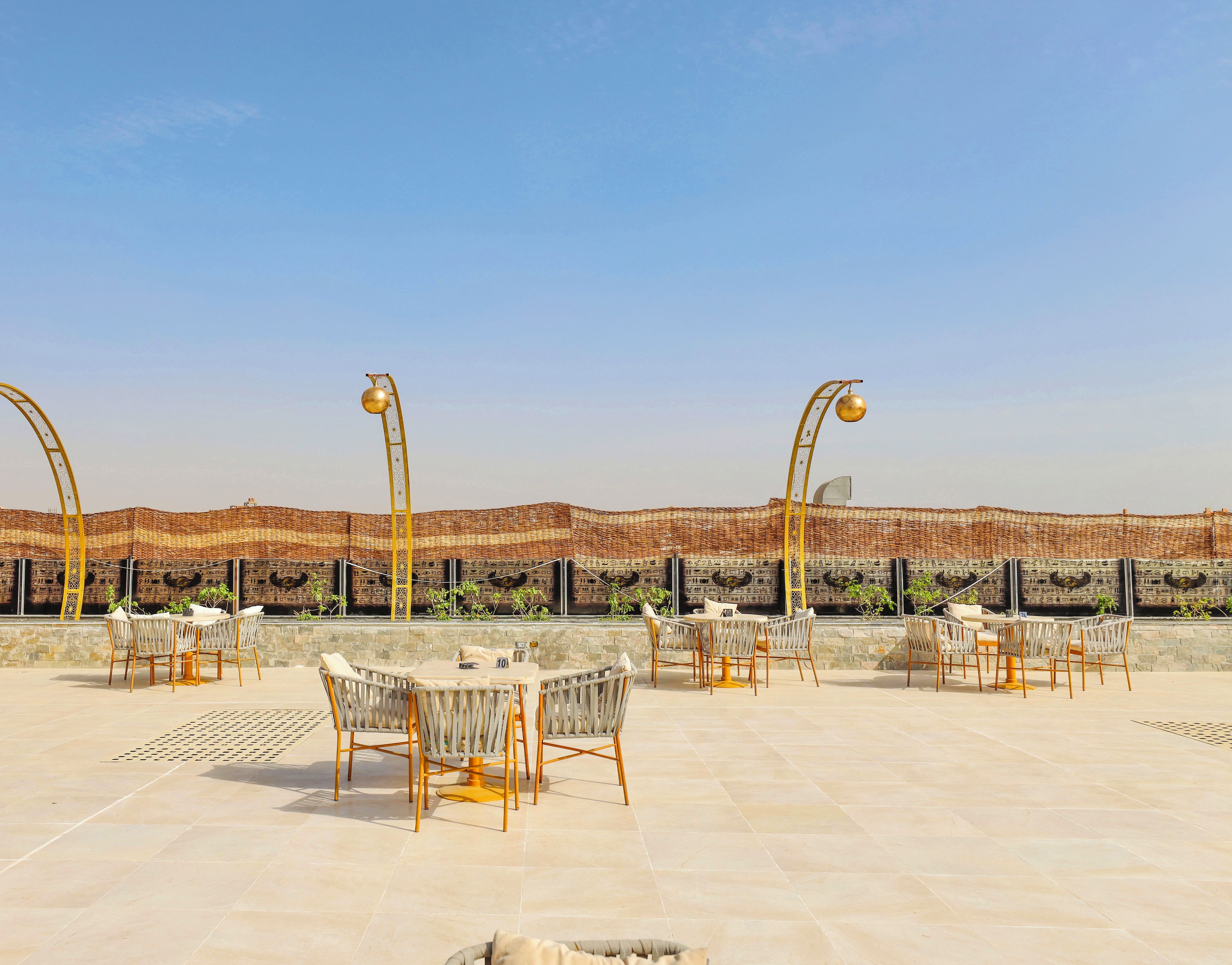 Un espace extérieur aménagé avec des tables et des chaises, une clôture décorative et un ciel dégagé.