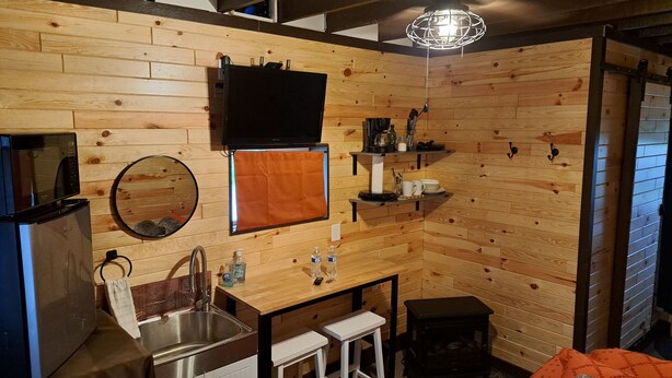 Cozinha compacta com pia, micro-ondas, geladeira, mesa pequena com banquinhos e ventilador de teto.