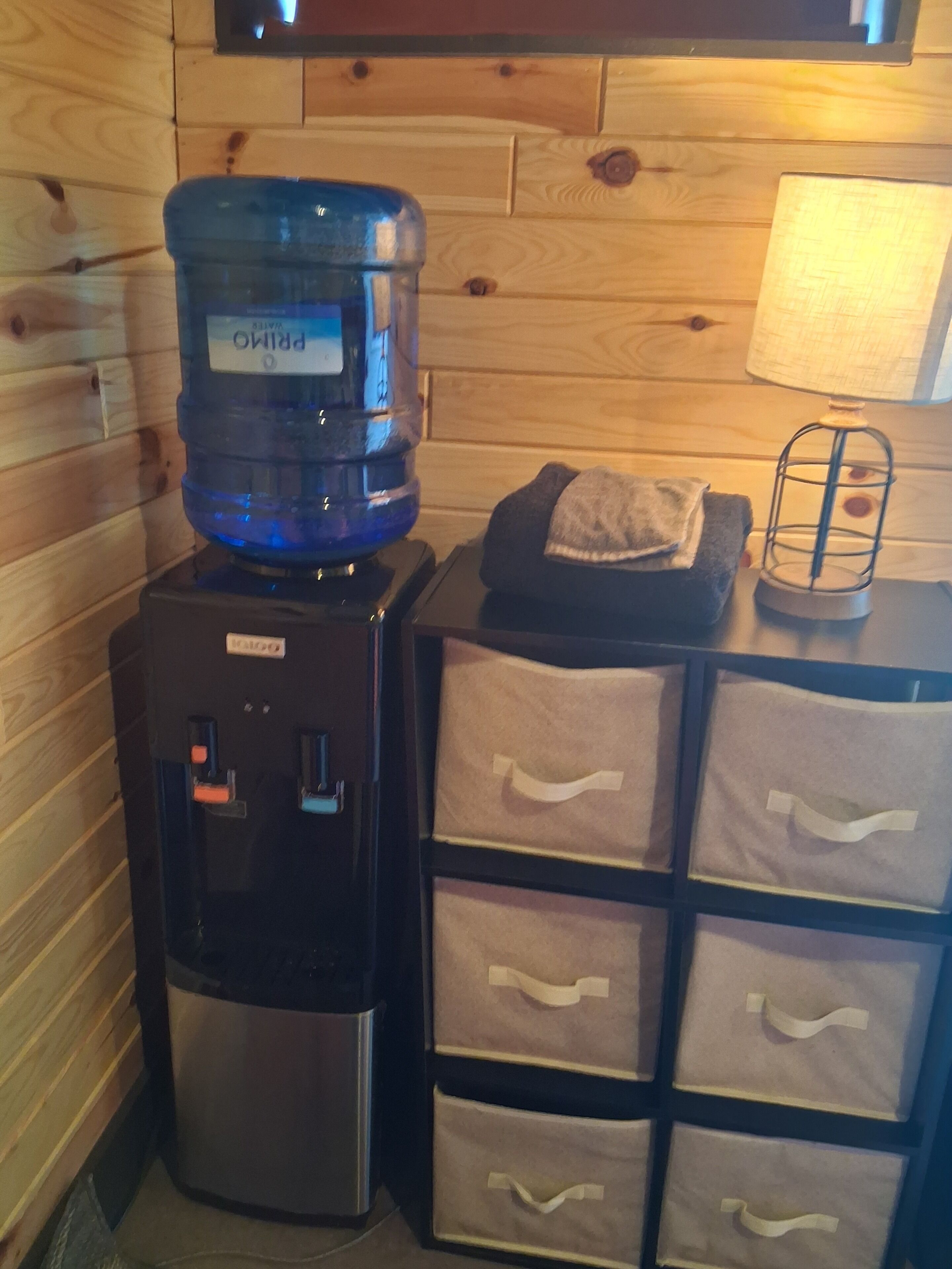 A water dispenser, a lamp, and storage drawers in a room with wooden walls.