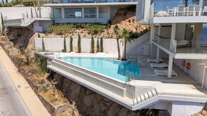 A modern hotel with a swimming pool, a staircase leading to a rooftop terrace, and a view of the surrounding landscape.