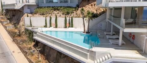 A modern hotel with a swimming pool, a staircase leading to a rooftop terrace, and a view of the surrounding landscape.