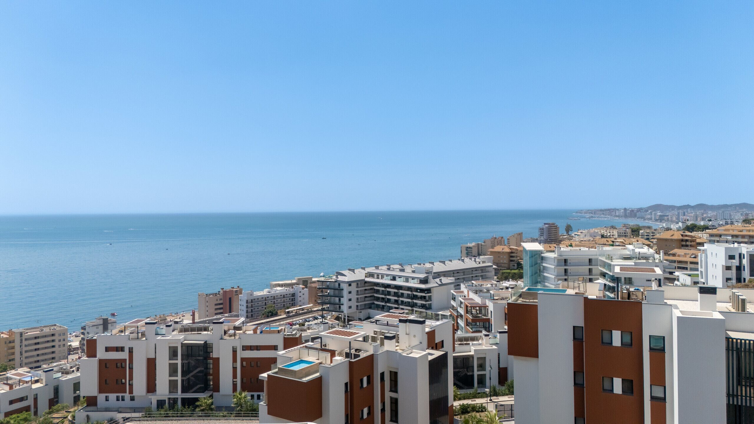 A coastal cityscape with modern buildings, a clear sky, and the sea in the background.