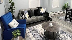 A modern living room with a grey sofa, blue armchair, and a round coffee table. - Cozy 2-bedroom apartment in charming New Britain with WiFi (New Britain)