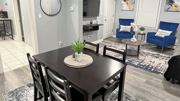 A modern living room with a dark wooden dining table, blue sofas, and a flat-screen TV mounted on the wall. - Cozy 2-bedroom apartment in charming New Britain with WiFi (New Britain)