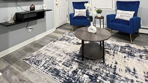 A modern living room with a flat-screen TV mounted on the wall, two blue armchairs with 'welcome home' pillows, a round coffee table, and a patterned rug. - Cozy 2-bedroom apartment in charming New Britain with WiFi (New Britain)