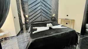 A modern hotel room with a marble-patterned floor, a black bed with a unique headboard design, and a bedside table with a lamp. - AT THE NAPLES TRACK CAMERA GOLD (Napoli)