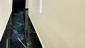 A modern hallway with a black marble floor, white walls, and a dark door at the end. - AT THE NAPLES TRACK CAMERA GOLD (Napoli)