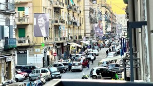 A busy urban street with multi-story buildings, parked cars, and pedestrians. - AT THE NAPLES TRACK CAMERA GOLD (Napoli)