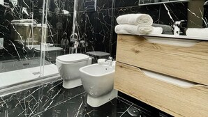 A modern bathroom with a black marble floor, a glass shower enclosure, a toilet, a bidet, and a wooden vanity with a mirror. - AT THE NAPLES TRACK CAMERA GOLD (Napoli)