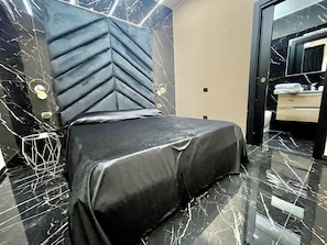Una camera da letto moderna con un letto, uno specchio e un bagno visibile attraverso una porta aperta.