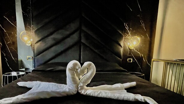 A bed with a towel arranged in a heart shape, a modern headboard, and two bedside lamps. - AT THE NAPLES TRACK CAMERA GOLD (Napoli)