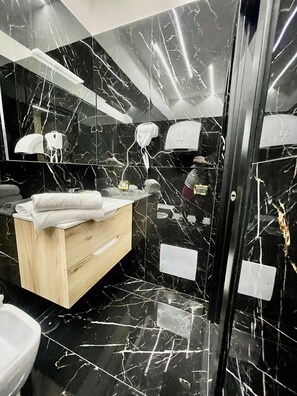Un bagno moderno con pareti in marmo nero, un mobile vanitario in legno e uno specchio.