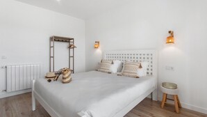A bedroom with a bed, a radiator, a wooden ladder, a small stool, and two wall-mounted lights.