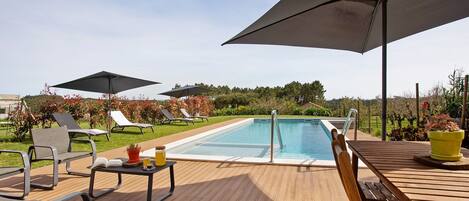 A poolside area with lounge chairs, umbrellas, a wooden deck, and a pool.