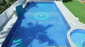A rectangular swimming pool with a tiled pattern, surrounded by a concrete deck and a grassy area. - Hotel Priso (Puducherry)