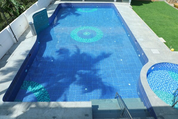 Une piscine rectangulaire dont le fond est recouvert de carreaux, entourée d’une terrasse en béton et d’une pelouse.