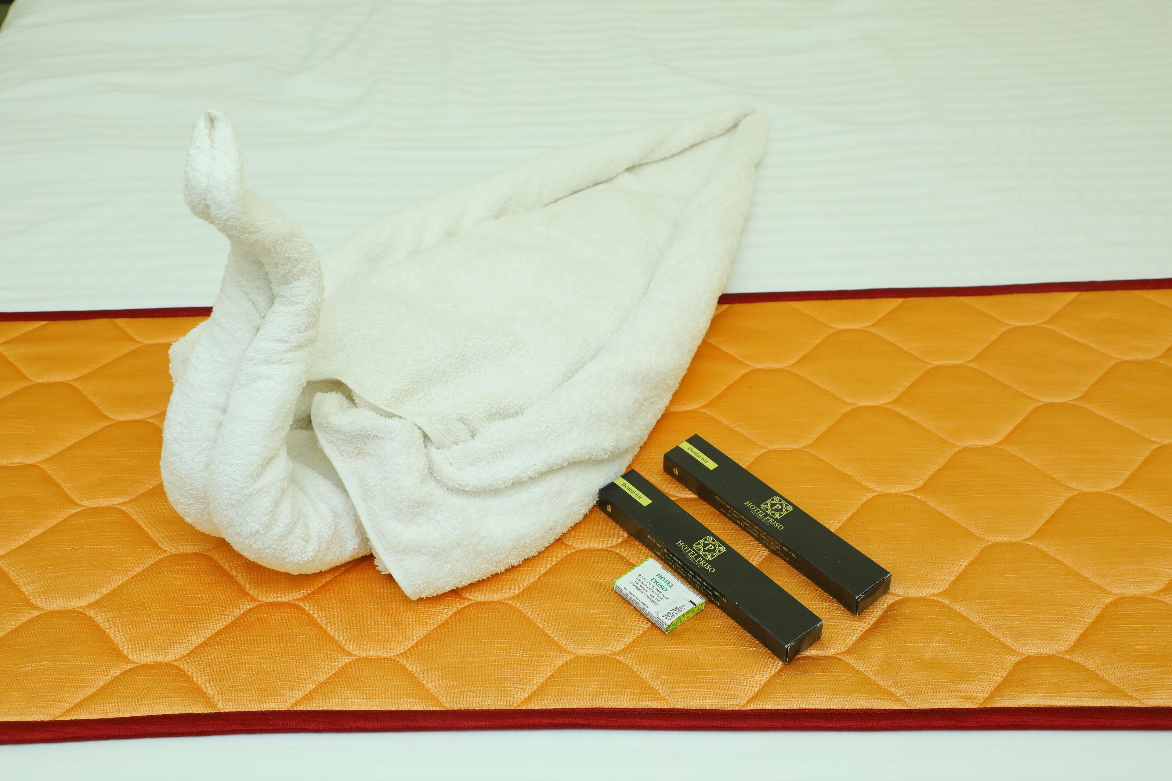 A bed with a white sheet, an orange mattress cover, and two black items on the bed.