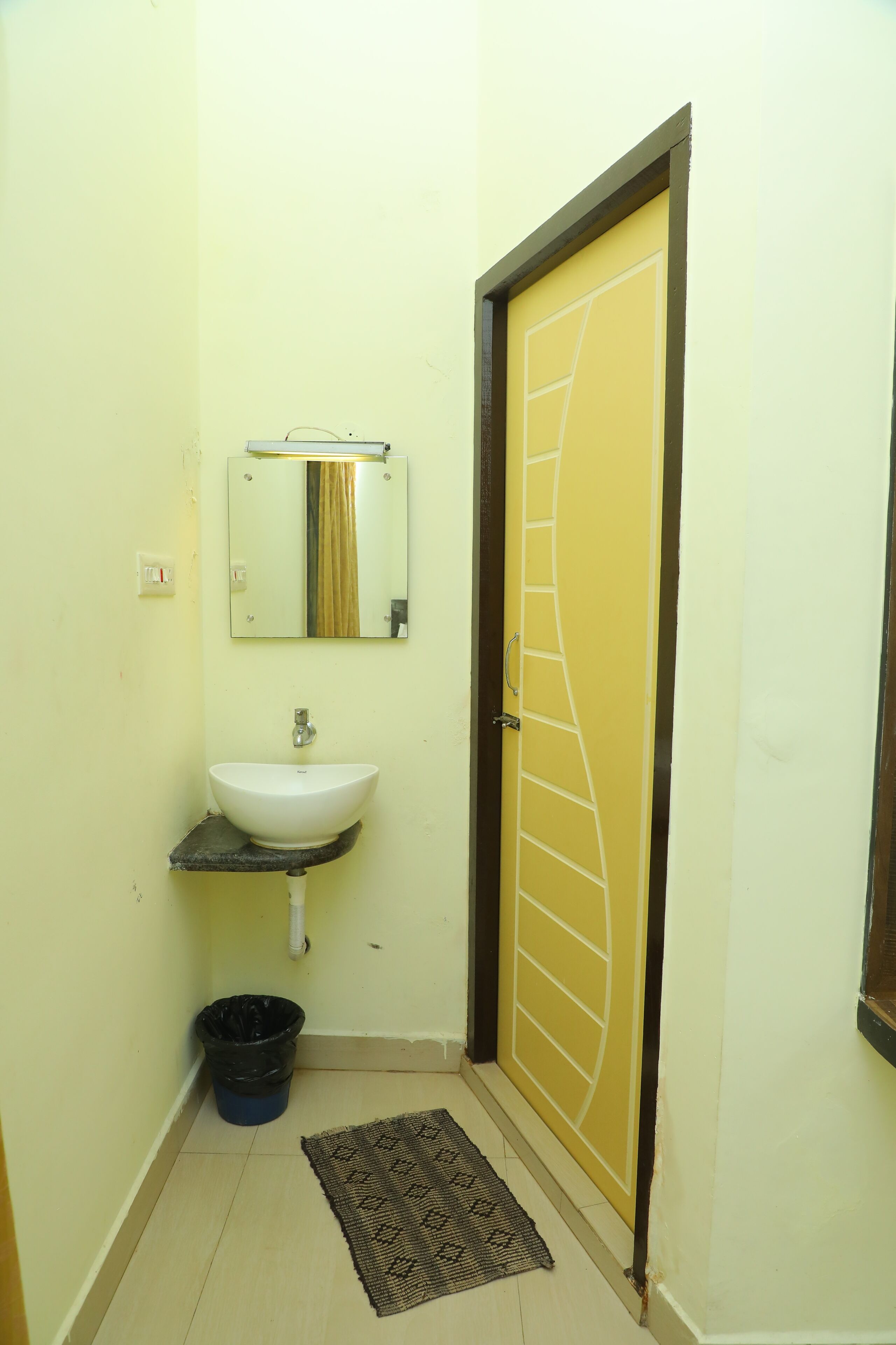 A bathroom with a white sink, a mirror, a black trash bin, and a patterned mat on the floor.