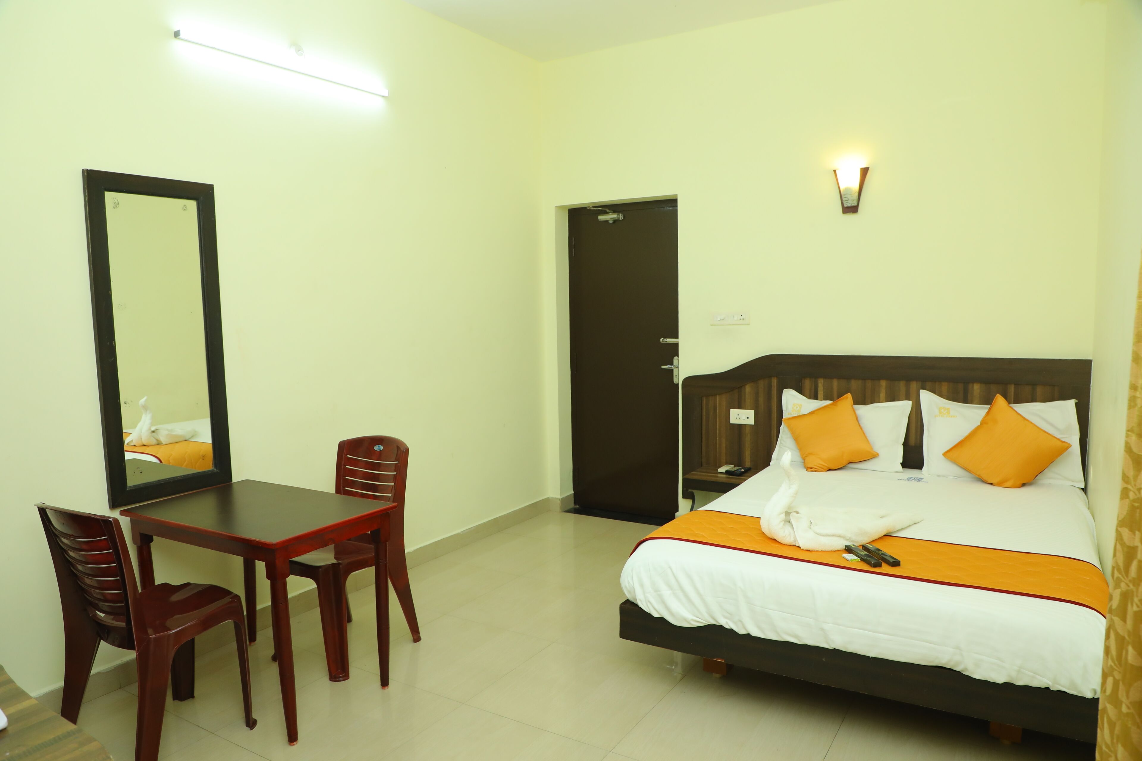 A hotel room with a bed, a desk, chairs, a mirror, and a door.