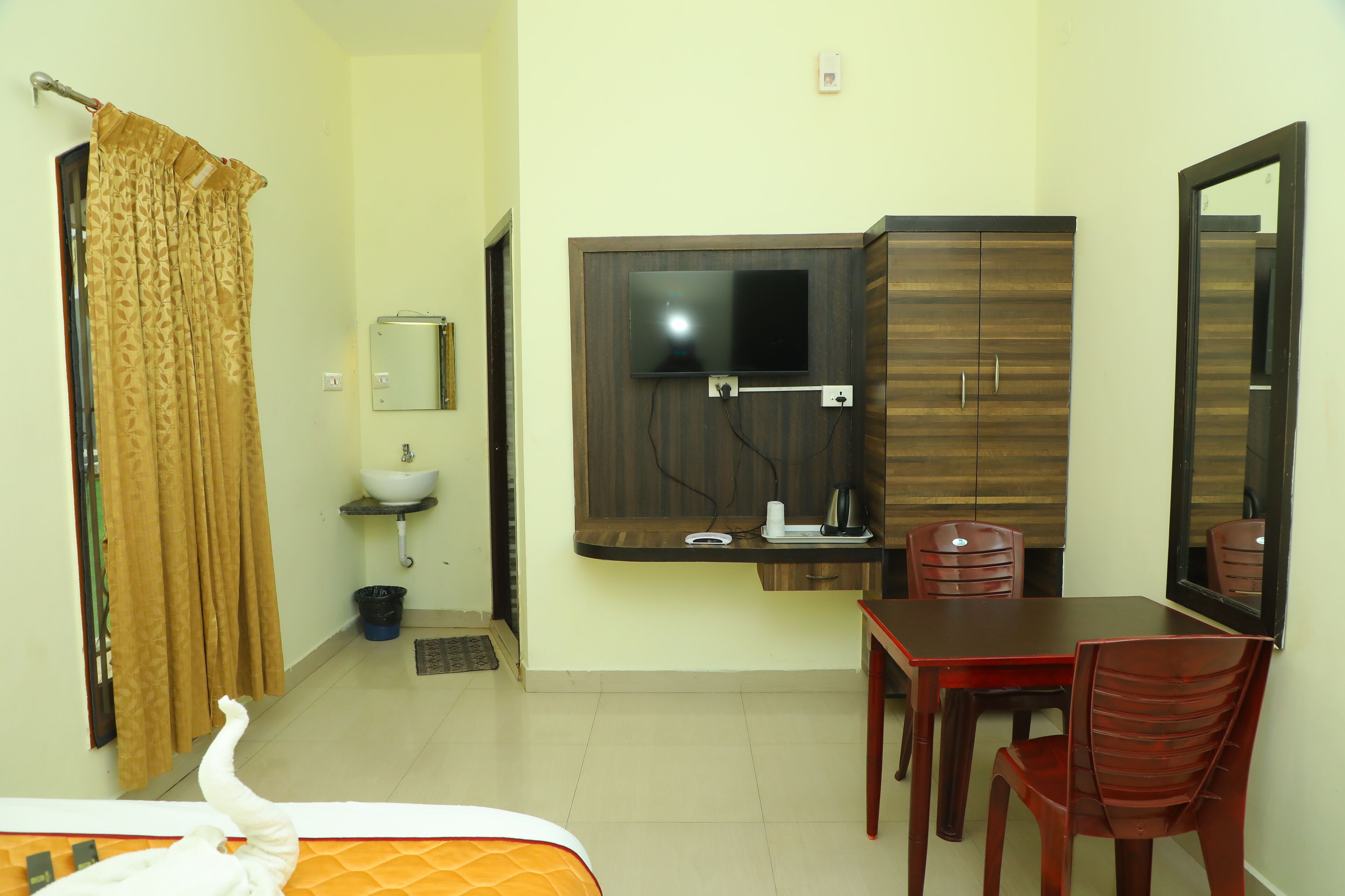 Habitación de hotel con cama, escritorio, silla, televisor, espejo, lavamanos y cortina.