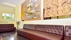 A modern lobby with a brown leather sofa, a large decorative wall piece, and a fan. - Hotel Priso (Puducherry)