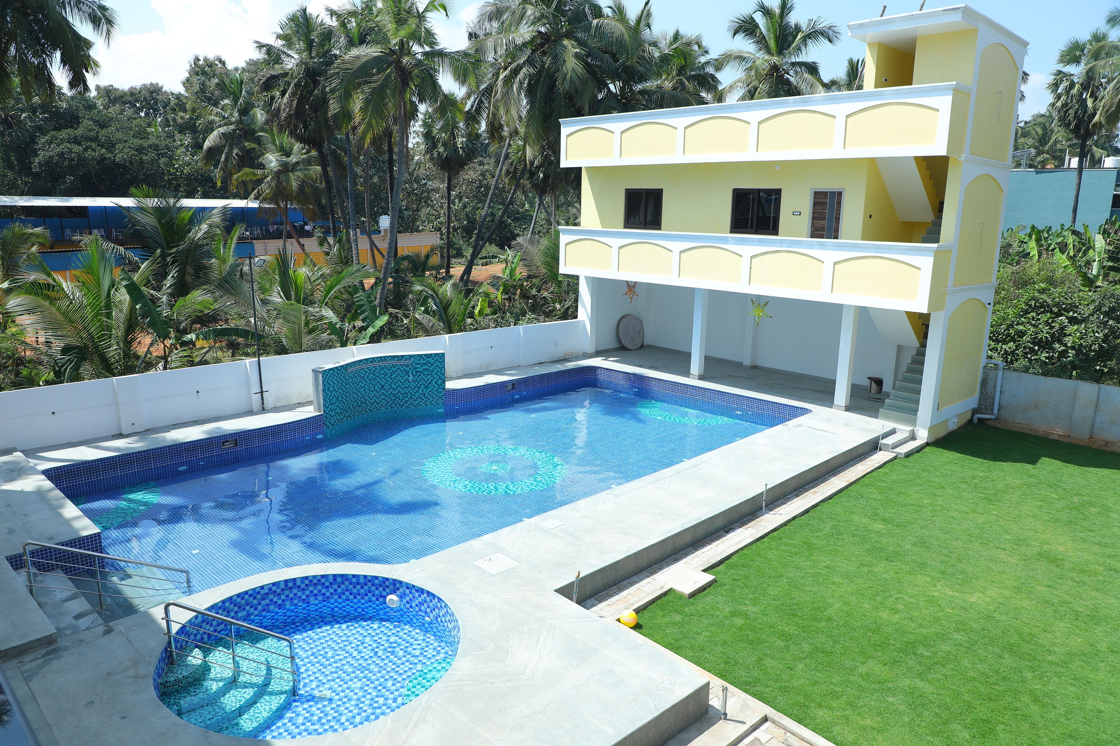 A swimming pool with a tiled deck, a two-story building with balconies, and surrounding palm trees.