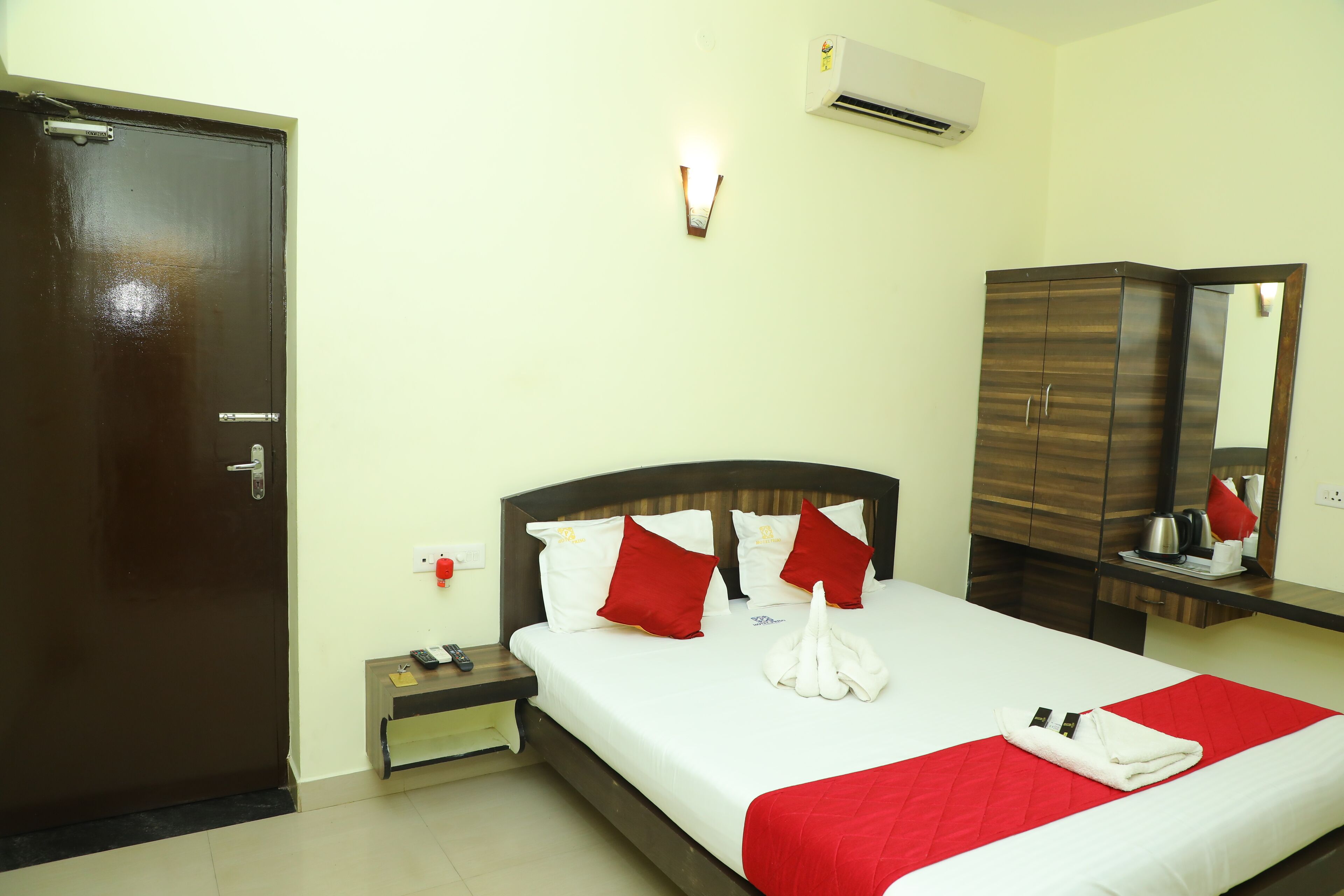 A hotel room with a bed, a wardrobe, a nightstand, a wall-mounted light, and an air conditioning unit.