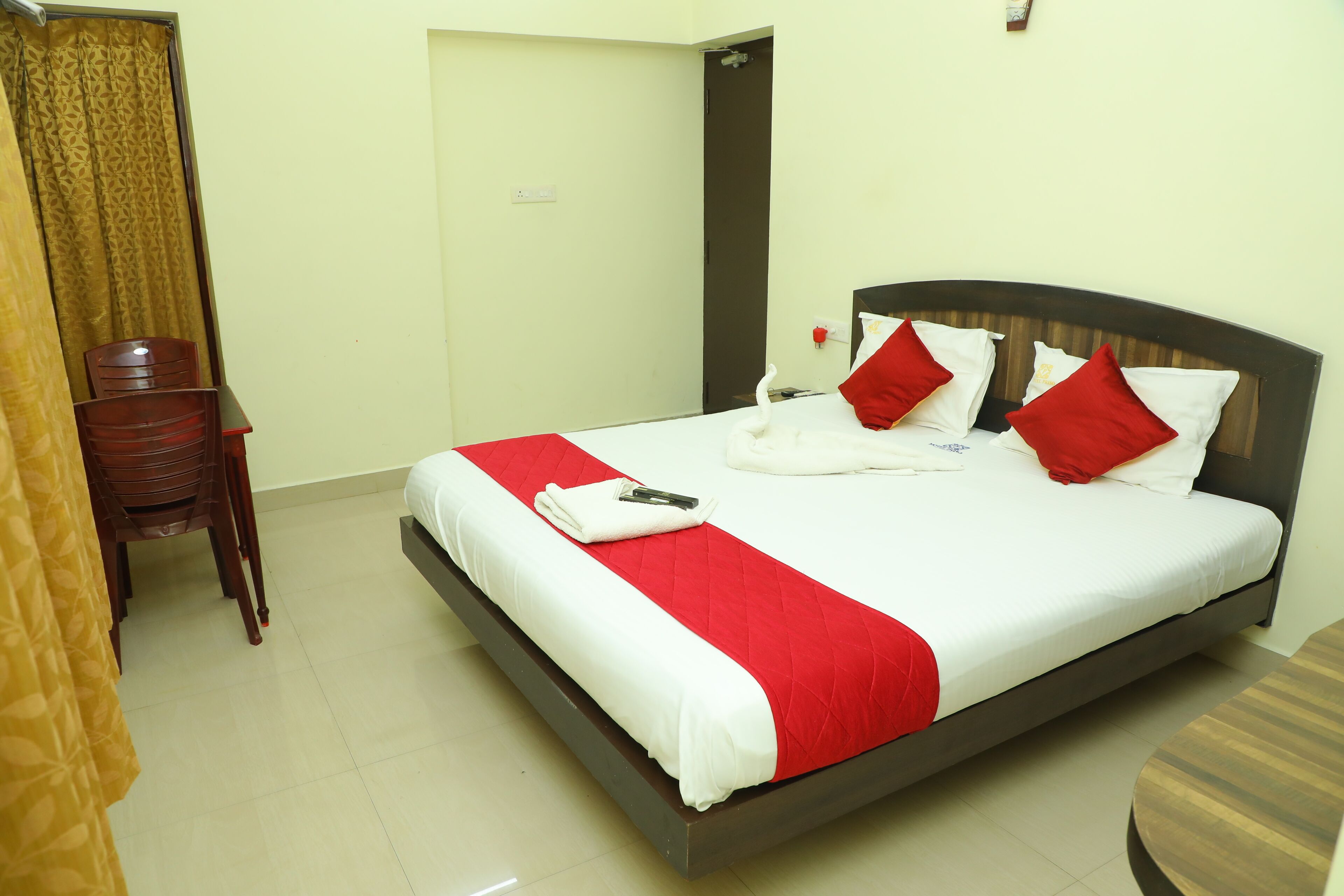 A hotel room with a bed, a chair, a small table, and a curtain.