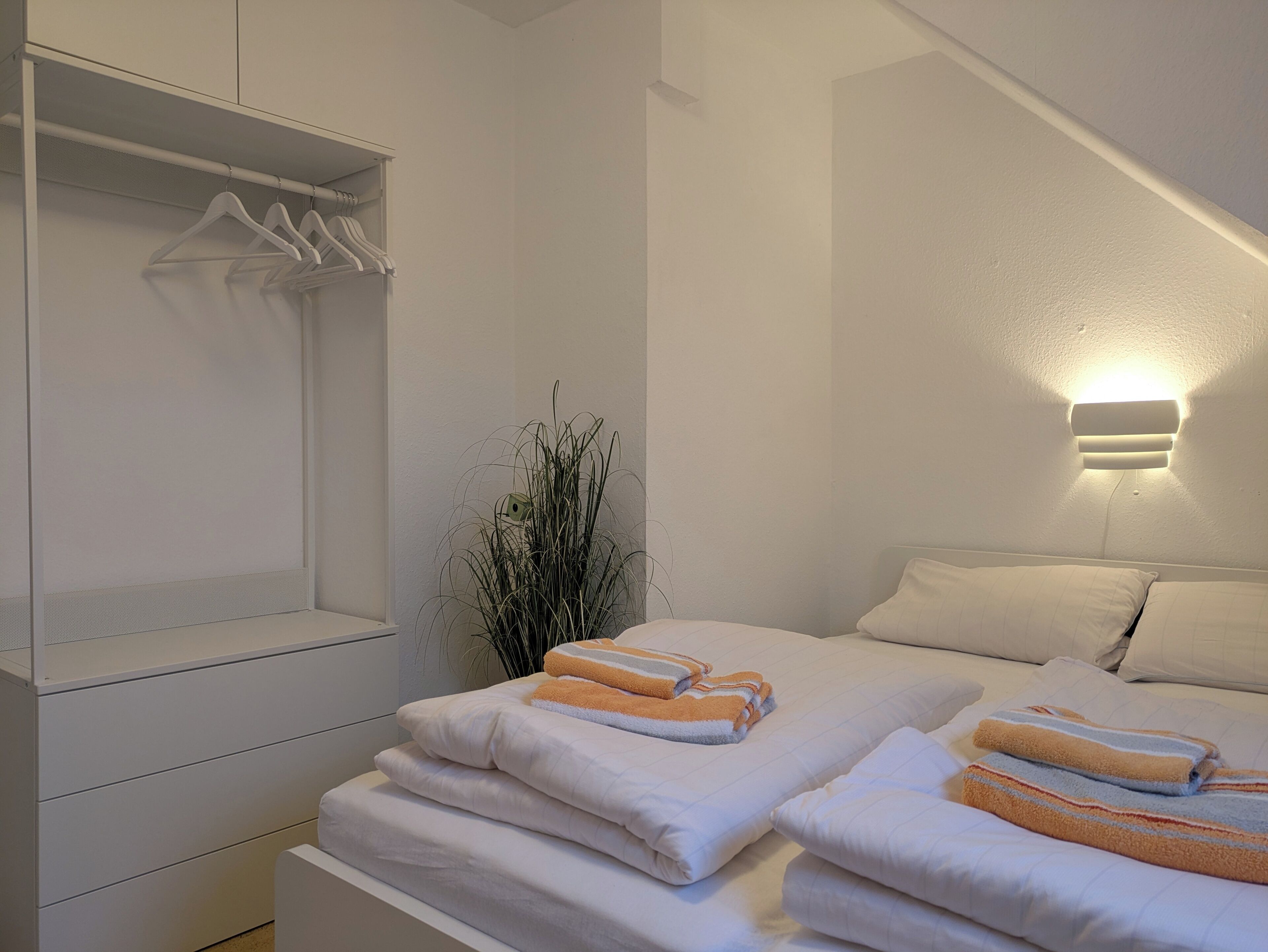 A hotel room with a bed, a bedside table, a wardrobe, and a wall-mounted light fixture.