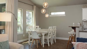 A dining area with a white table and chairs, a hanging light fixture, and a window with curtains.