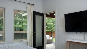 A bedroom with a bed, a TV mounted on the wall, and a door leading to an outdoor patio with a chair and table.