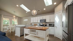 A modern kitchen with white cabinets, a wooden island, stainless steel appliances, and a dining area with a white table and chairs.