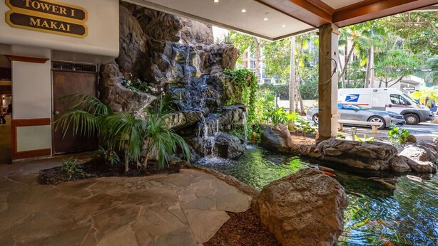Un hall d’hôtel agrémenté d’une cascade, un comptoir d’accueil et un panneau indiquant « Tour I Makai ».