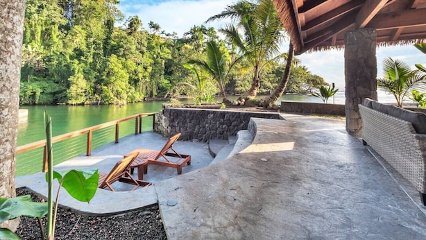 Un espacio al aire libre de estilo tropical con un muro de piedra, una mesa de madera y sillones de descanso.