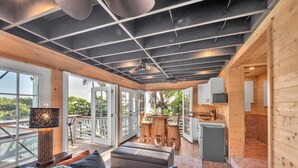 Un interior moderno con techo de madera, un sofá con cojines, una mesa de comedor y una zona de cocina.