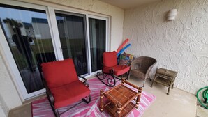 Un balcón con una silla roja, una silla de mimbre, una mesita y un tapete estampado.