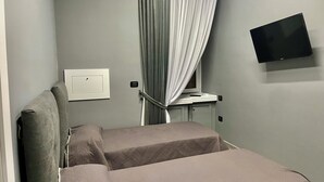 Habitación de hotel con dos camas, un televisor de pantalla plana, aire acondicionado, una ventana con cortinas y una mesita de noche con lámpara.